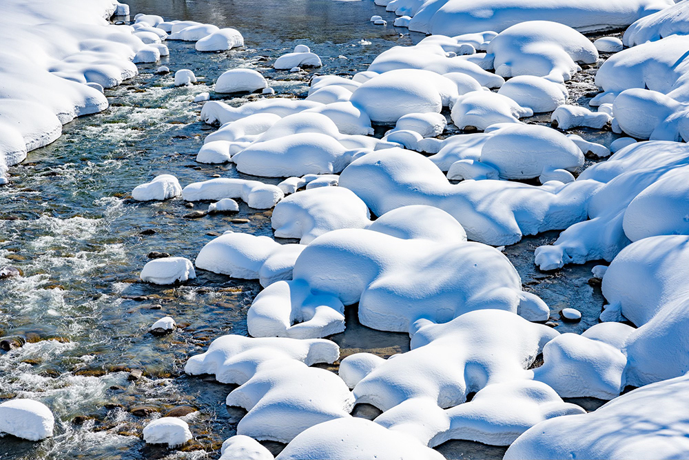 河原の石に積もる雪綿帽子