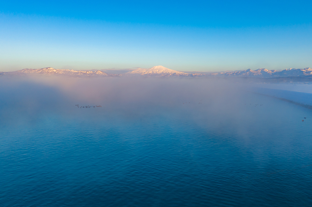 朝靄が漂い、ため池と鳥海山が繋がっているように見える